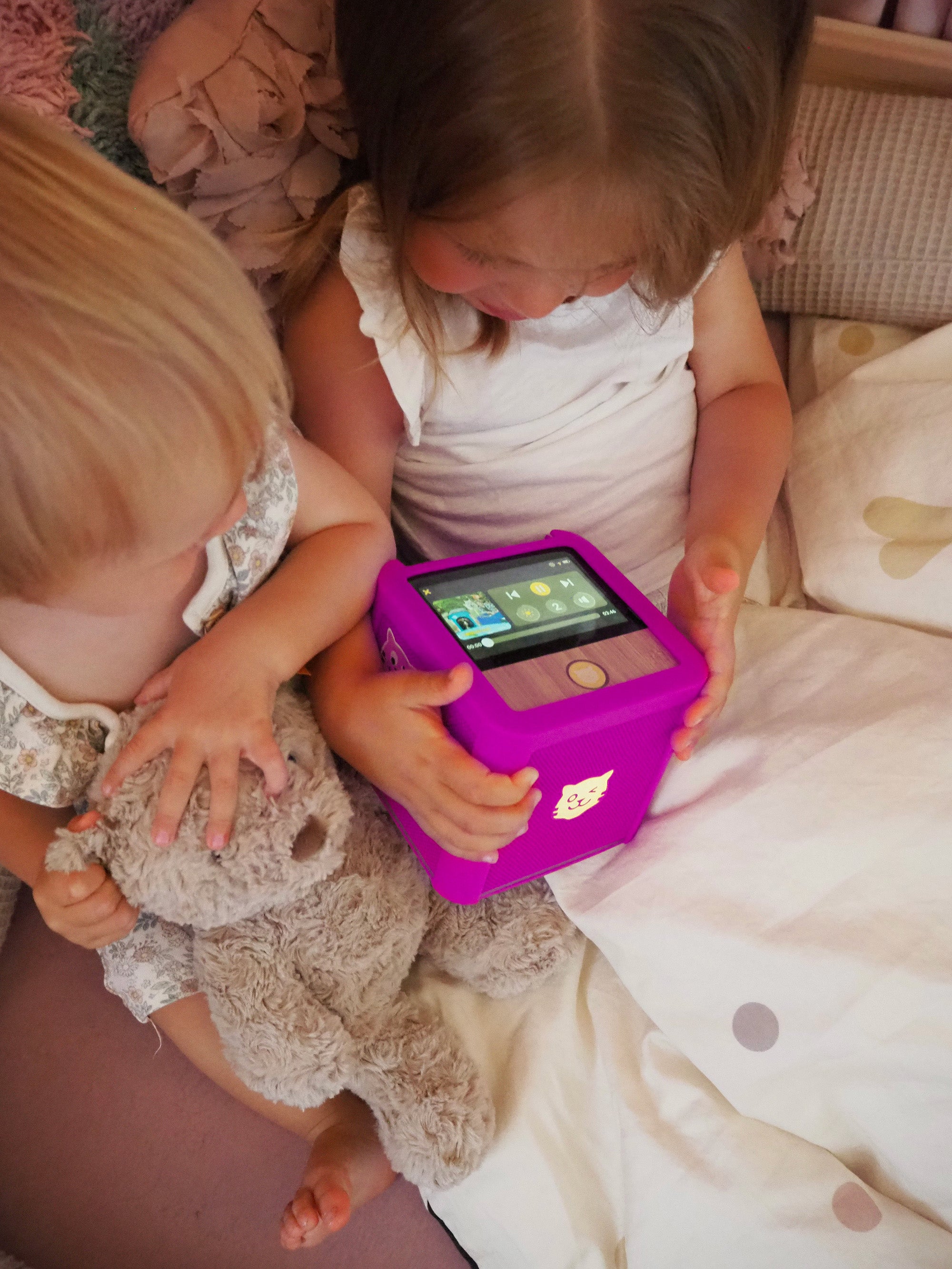 Zwei Kinder genießen Hörspielzeit mit der tigerbox TOUCH, eingehüllt in eine Decke, und mit einem Kuscheltier an ihrer Seite.