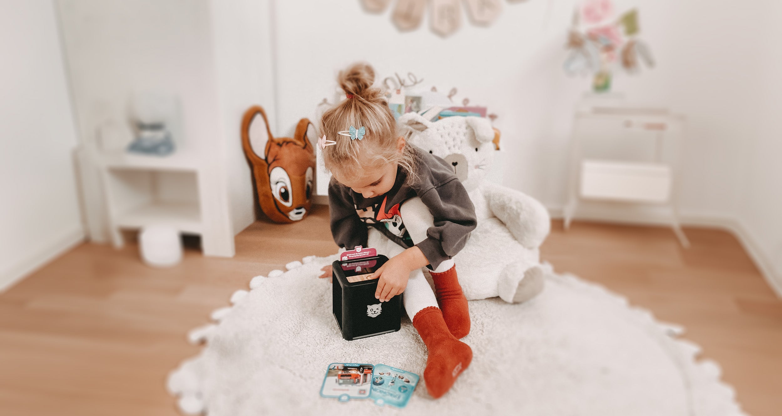 Mit der tigerbox TOUCH im Kinderzimmer – ein Mädchen startet ein Hörspiel mit tigercard, weitere tigercards liegen neben der Box.